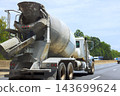 Concrete mixer truck drives along highway near tree line under bright daytime sky. 143699624