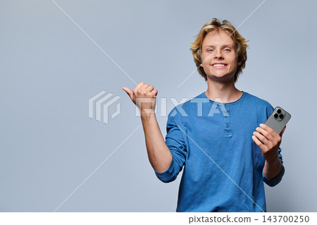 Young man holding smartphone pointing aside at copy space in gray studio Young man holding smartphone pointing aside at copy space in gray studio 143700250