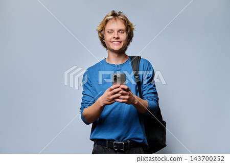 Happy young male student holding smartphone with backpack on grey studio background Happy young male student holding smartphone with backpack on grey studio background 143700252