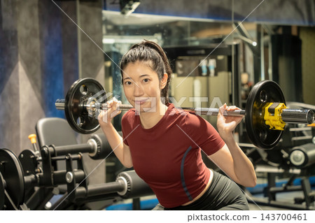 一名女子肩扛槓鈴做深蹲。 一名女子肩扛槓鈴做深蹲。 143700461