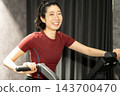 一位女士面帶微笑，緊緊握住健身自行車的車把。 143700470