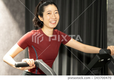 一位女士面帶微笑,緊緊握住健身自行車的車把。 一位女士面帶微笑,緊緊握住健身自行車的車把。 143700470