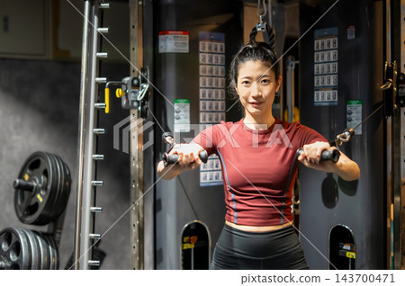 一名女子在健身房伸展面前的纜繩訓練器把手。 143700471