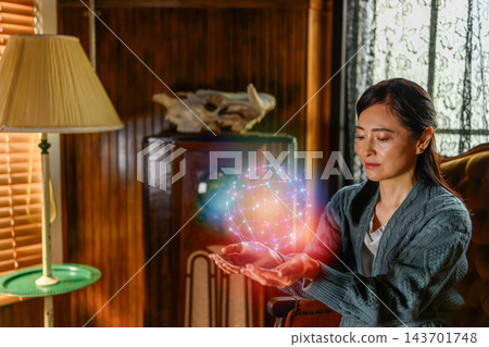 房間裡,一名女子雙手捧著一個發光的球狀全息圖。 房間裡,一名女子雙手捧著一個發光的球狀全息圖。 143701748