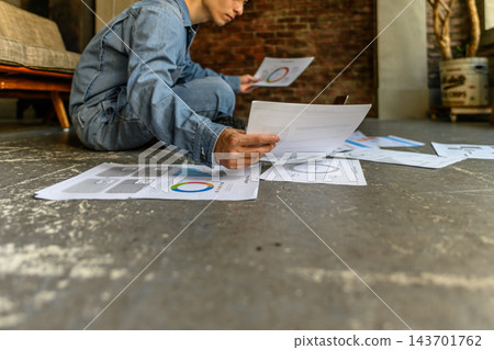 一名男子在地板上工作,同時查看文件中的圖表。 一名男子在地板上工作,同時查看文件中的圖表。 143701762