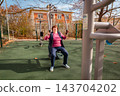 Senior Caucasian woman training in a sunny park on gym machines. Health, energy, and long life concept. 143704202