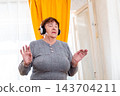 Portrait of older woman dancing with closed eyes and enjoying music indoors. Calm atmosphere and positivity. Concept of relaxation for seniors. 143704211