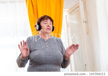Portrait of older woman dancing with closed eyes and enjoying music indoors. Calm atmosphere and positivity. Concept of relaxation for seniors. 143704211