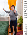 Older Caucasian woman listening to relaxing music and moving gently indoors. Calm mood and comfort. Concept of wellness for seniors. Vertical 143704213