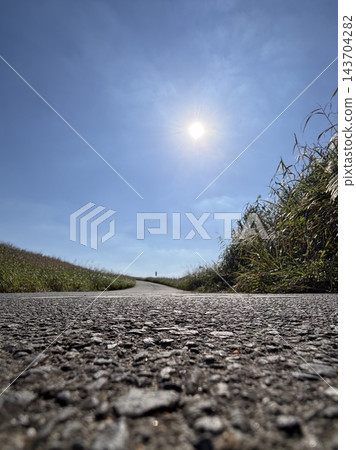 低角度拍攝的柏油路穿過草地延伸至遠方,背景是湛藍的天空。 低角度拍攝的柏油路穿過草地延伸至遠方,背景是湛藍的天空。 143704282