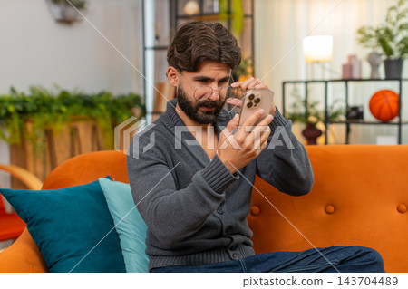 Indian man with eyeglasses squints at smartphone screen tries to read small text poor vision focus Indian man with eyeglasses squints at smartphone screen tries to read small text poor vision focus 143704489
