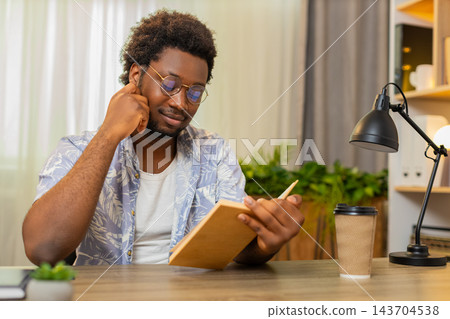 African American young man on home table reads book with focus and learns new ideas for self growth 143704538