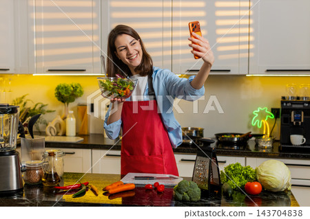 Young woman showing fresh salad on smartphone video call in home kitchen for healthy diet lifestyle 143704838
