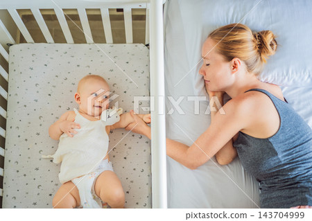 Woman tending to her infant while resting beside the baby's crib. Woman tending to her infant while resting beside the baby's crib. 143704999
