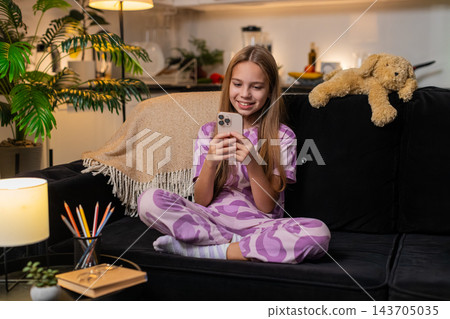 Teenager girl texting reply after happy message from friend on smartphone smiling chat app at night Teenager girl texting reply after happy message from friend on smartphone smiling chat app at night 143705035