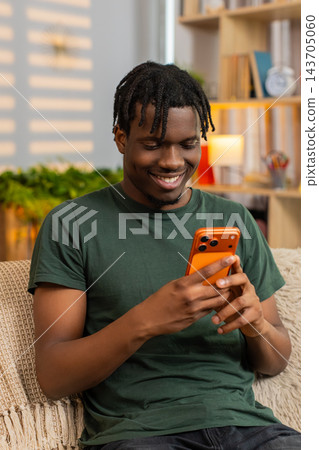 African American young man on home sofa reading smartphone message with relaxed happy smile indoors African American young man on home sofa reading smartphone message with relaxed happy smile indoors 143705060