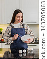Young woman cracking eggs in kitchen bowl preparing simple breakfast omelet or baking dough at home 143705063