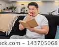 Asian man bites red apple enjoys juicy taste and read short health tips in book with calm smile well 143705068