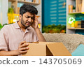 Indian man on home sofa opening parcel finding wrong product with upset face during online shopping 143705069