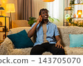 African American young man on home sofa enjoys a pleasant smartphone call with friendly conversation 143705070