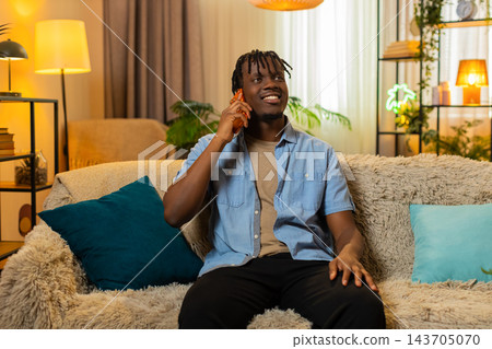 African American young man on home sofa enjoys a pleasant smartphone call with friendly conversation African American young man on home sofa enjoys a pleasant smartphone call with friendly conversation 143705070
