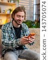 Young man on home sofa reading smartphone message with worry then smiling with relief in living room 143705074