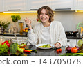 Young woman eating fresh salad in kitchen with happy smile during healthy diet lunch for self care 143705078
