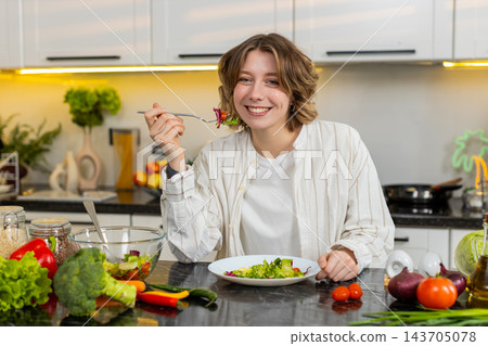 Young woman eating fresh salad in kitchen with happy smile during healthy diet lunch for self care Young woman eating fresh salad in kitchen with happy smile during healthy diet lunch for self care 143705078