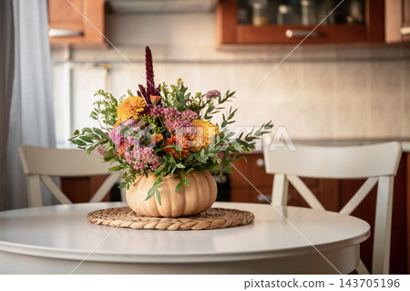 Autumn flower arrangement in pumpkin vase on kitchen table Autumn flower arrangement in pumpkin vase on kitchen table 143705196