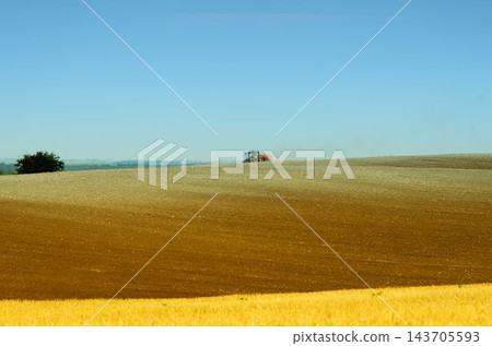 Tractor Plowing Rural Farmland Under Clear Blue Sky Tractor Plowing Rural Farmland Under Clear Blue Sky 143705593