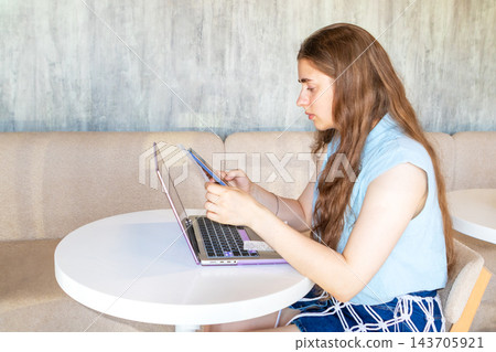 Young woman using laptop and tablet at a cafe table, studying and multitasking with technology 143705921