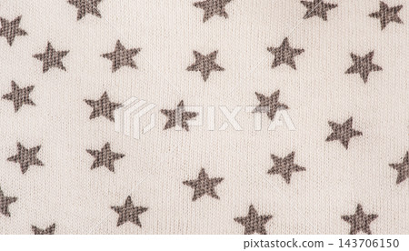 Knitted fabric of light beige color in gray stars. Macro photo of clothes as a background. 143706150