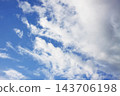 White cumulus and wispy cirrus clouds spread across a blue sky. 143706198