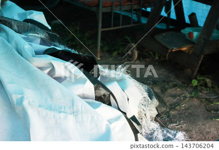 An old metal bed with a wire mesh frame and curved headboards stands among discarded items in an outbuilding. An old metal bed with a wire mesh frame and curved headboards stands among discarded items in an outbuilding. 143706204