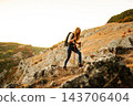 Woman hiking rocky mountain trail using trekking poles 143706404