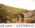 Woman backpacking uphill on a rocky path with trekking poles 143706410
