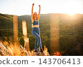 Young woman celebrating success reaching mountain peak at sunset 143706413