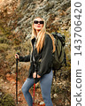 Young adult woman hiking in mountains with backpack and trekking poles 143706420