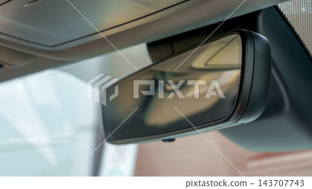 Close up of a vehicle rearview mirror reflecting the interior roof and seats inside a modern car cabin 143707743