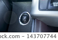 Close up of illuminated engine start stop button with chrome trim beside dark textured dashboard in a modern vehicle interior 143707744