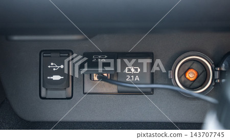 Close up view of vehicle dashboard with USB port, power socket, charging adapter, and connected cable in dark interior Close up view of vehicle dashboard with USB port, power socket, charging adapter, and connected cable in dark interior 143707745