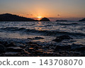 夕陽西下，海面波光粼粼，海浪輕拍著岩石海岸。 143708070