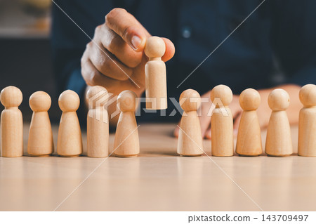 Hand lifts one wooden figure above a row of people, symbolizing recruitment, talent selection, promotion, leadership, hiring, career advancement, employee recognition, opportunity, and success. 143709497