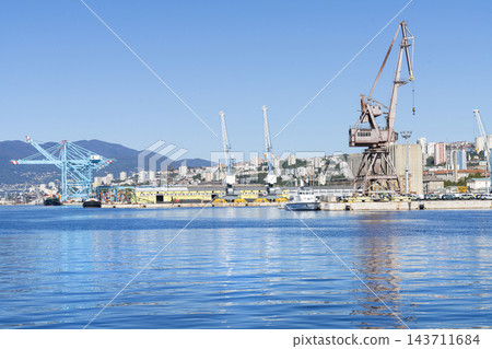A large blue gantry crane and a rusty industrial crane are prominent features at the busy harbor of Rijeka, Croatia A large blue gantry crane and a rusty industrial crane are prominent features at the busy harbor of Rijeka, Croatia 143711684