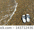 A single sandal is lined up on the shoreline of a beach covered with pebbles. 143712436