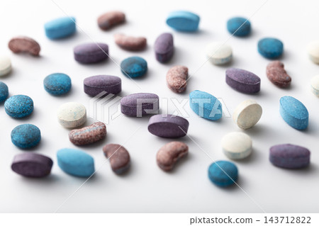 Assorted colorful medicinal pills and vitamin supplements scattered on a clean white surface Assorted colorful medicinal pills and vitamin supplements scattered on a clean white surface 143712822