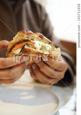 Person holding a sandwich with tomato and cheese at a cafe table Person holding a sandwich with tomato and cheese at a cafe table 143712938