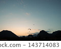 一架滑翔傘在寮國的傍晚天空中翱翔，周圍環繞著山脈。 143714083