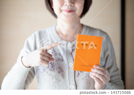 中老年婦女指著一本橘色的退休金手冊 中老年婦女指著一本橘色的退休金手冊 143715086