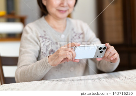 中老年女性在家裡的客廳用智慧型手機看影片。 143716230